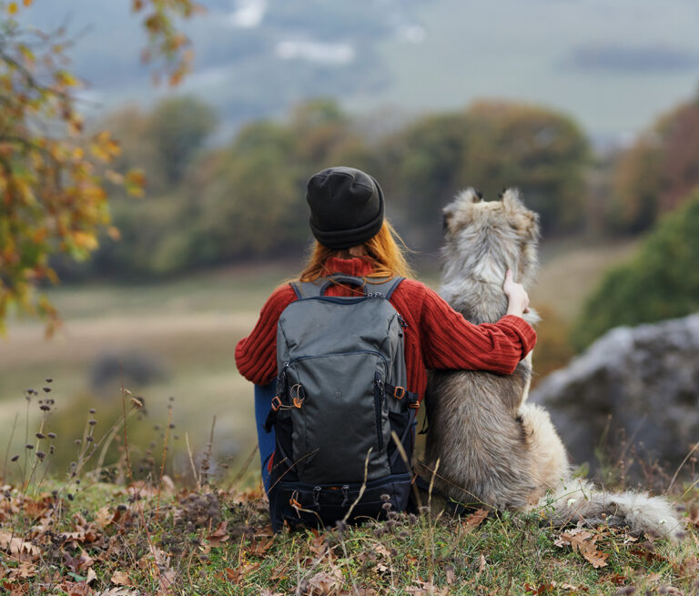 Frau mit Hund rastet beim Wandern in der herbstlichen Natur